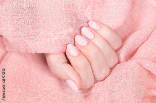 Closeup top view of pastel pink polished nail. Female hand holding soft pink material as background. Horizontal color photography.