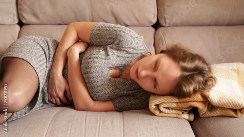 Unhappy woman having stomachache lying on couch at home photo