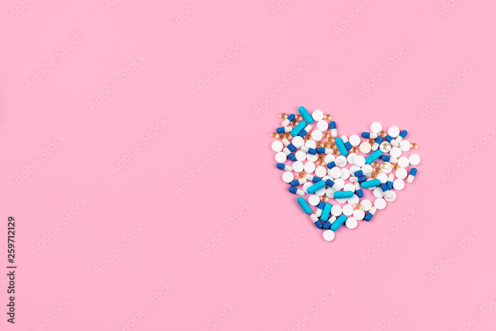 Bright blue and white pills and tablets in heart shape on pink background. Medicines, drugs, pharmacy concept. Flat lay, top view, minimal style