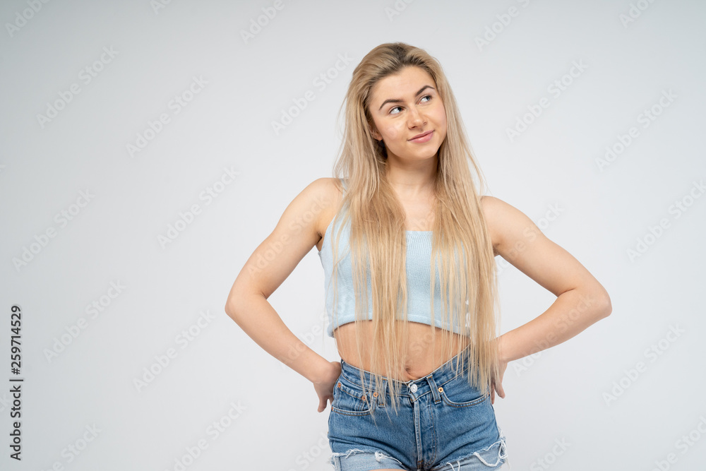 Young attractive girl smiles, stands hands on the sides and looks away. Isolated on white background Young attractive girl smiles, stands hands on the sides and looks away. Isolated on white background