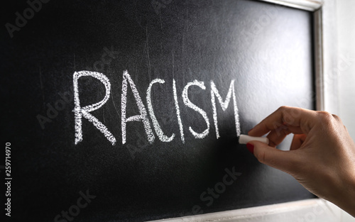 Hand writing the word racism on blackboard. Stop hate. Against prejudice and violence. Lecture about discrimination or stereotypes in school. photo