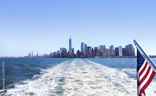 Lower Manhattan view from cruise ship or yacht with the flag of the United States of America in New York. Scenic view to NY Downtown and city centre. Staten Island Ferry. Tourists cruising in boat. photo