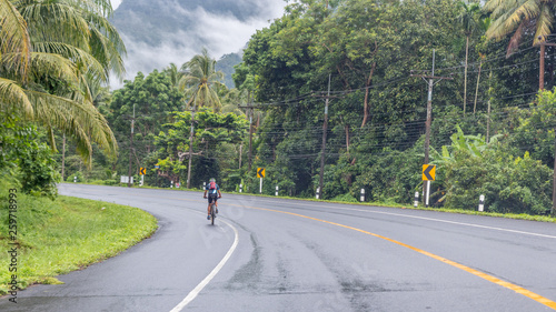 Man riding bicycle on highway in tropical rain forest in Thailand