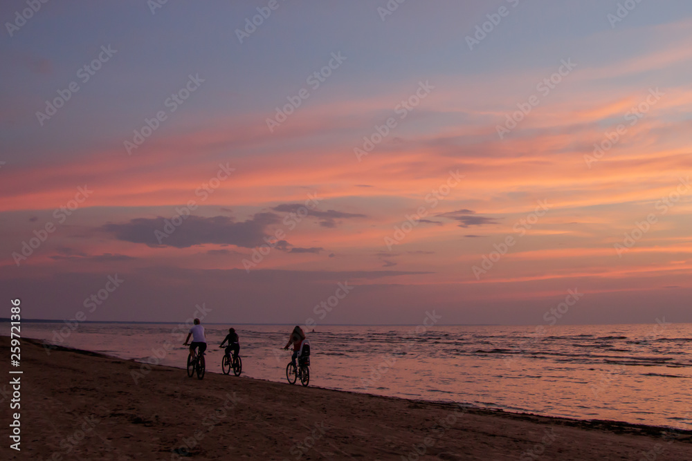 Three cyclists go away on the beach at sunset