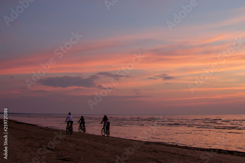 Three cyclists go away on the beach at sunset