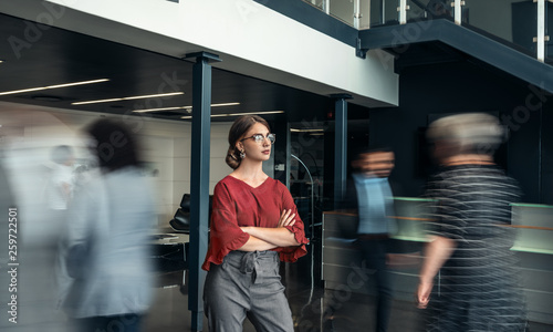 Photos Beautiful young business woman standing in a busy lobby of an office with her ar