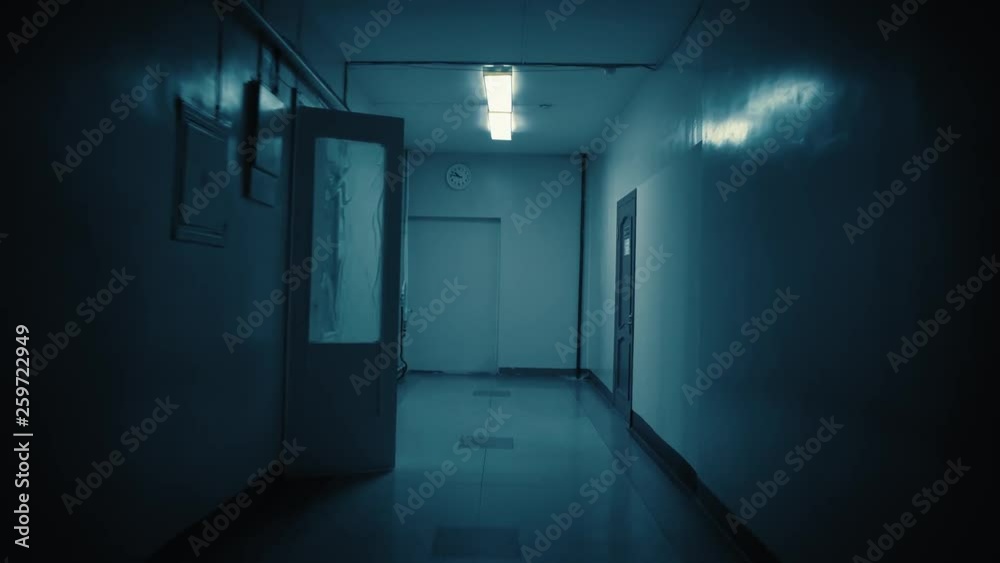 Tracking inside a long dark gloomy corridor, tunnel. On the wall at the end of the path there is a white big clock, it shows a quarter to eleven. Concept of horror.