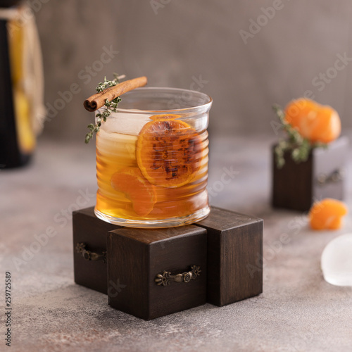 Whiskey sour cocktail with tangerine slices and ice cubes decorated with cinnamon and thyme. Alcohol drink background. photo