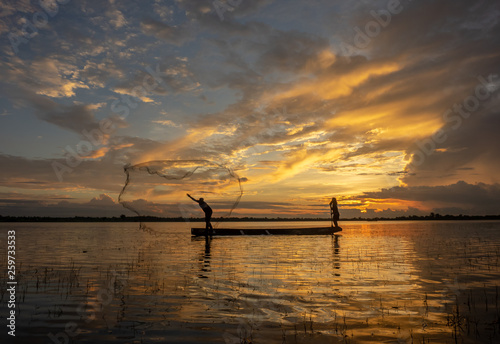 The silhouette fisherman casting a net into the water during on sunset 