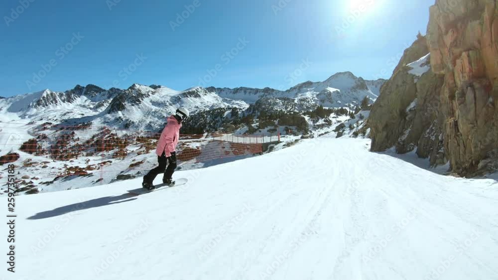 Young athletic woman extreme sports lover rides down wide open slope on snowboard, wears feminine pink winter jacket and protective helmet. Cold outdoors temperature vacation Young athletic woman extreme sports lover rides down wide open slope on snowboard, wears feminine pink winter jacket and protective helmet. Cold outdoors temperature vacation