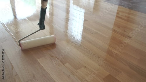 Varnishing lacquering parquet floor by paint roller - second layer. Home renovation parquet. Varnish paint roller strokes on a wooden parquet. Application of a highly glossy parquet lacquer