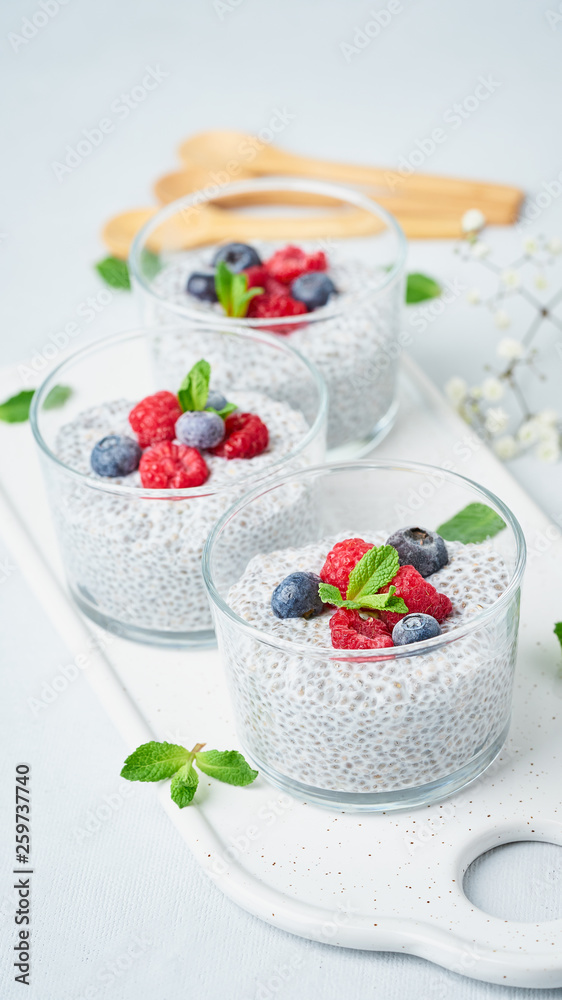 Chia pudding with fresh berries raspberries, blueberries. Three glass, vertical, light background, side view, flowers.