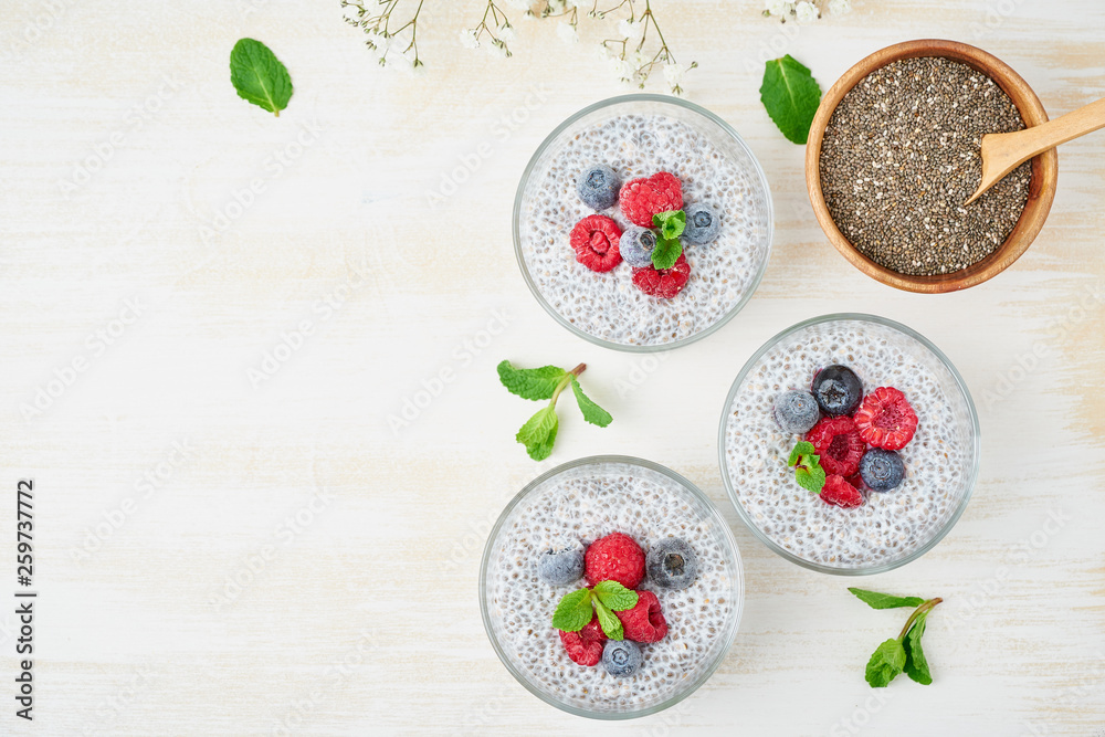 Chia pudding, top view, copy space, fresh berries raspberries, blueberries. Three glass, light wooden background, flowers, close up.