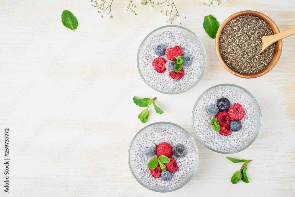 Chia pudding, top view, copy space, fresh berries raspberries, blueberries. Three glass, light wooden background, flowers, close up. Chia pudding, top view, copy space, fresh berries raspberries, blueberries. Three glass, light wooden background, flowers, close up.