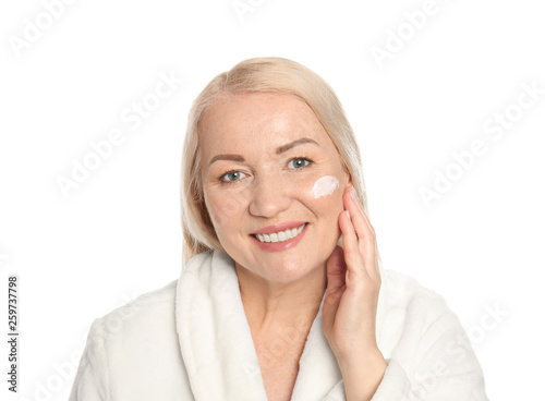 Mature woman applying facial cream on white background