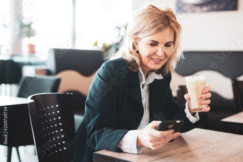 Attraktive ältere Frau sitzt im Cafe und checkt ihr Handy  photo