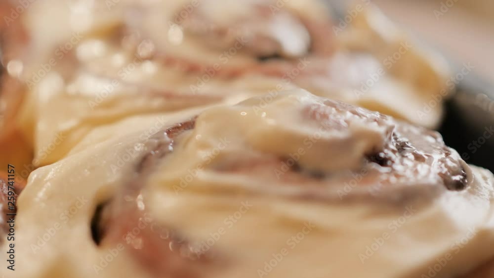 spreading a white creamy caramel cream on fresh hot cinnamon bun with spices in slow motion close up 4K video.