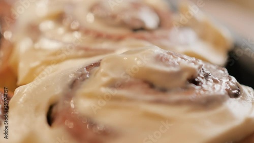 spreading a white creamy caramel cream on fresh hot cinnamon bun with spices in slow motion close up 4K video.