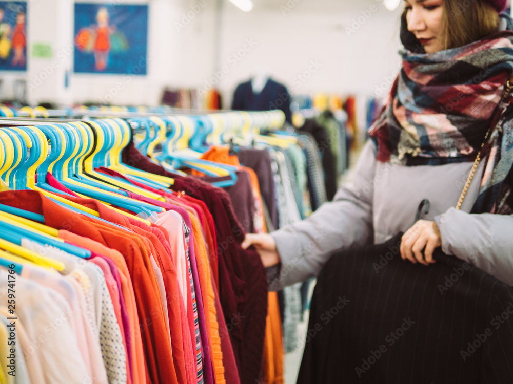 Young woman is browsing a rail of clothes at mall store