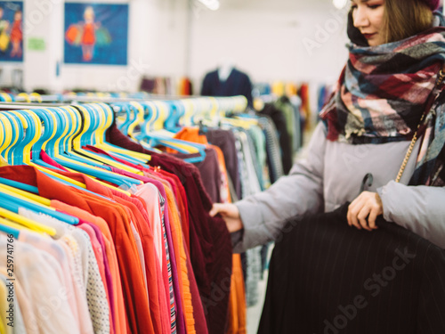 Young woman is browsing a rail of clothes at mall store