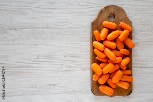 Fresh baby carrots on rustic wooden board on a white wooden table, top view. Overhead, from above, flat lay. Copy space. photo