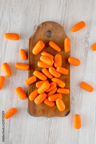Fresh baby carrots on rustic wooden board on a white wooden background, top view. Overhead, from above, flat lay.