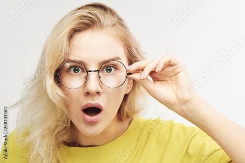 Surprised woman in round glasses with open mouth and bulging eyes looks into camera and sees something incredible and amazing isolated on white background photo