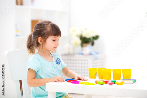 Little beautiful girl sculpts from plasticine at the table in the interior. Child development and fine motor skills. Children's creativity