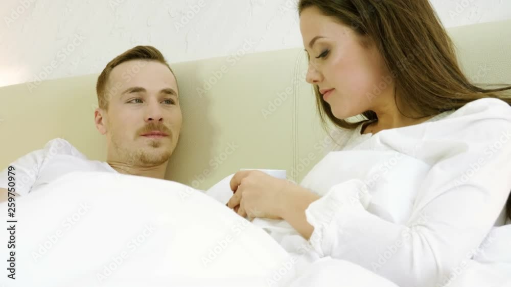 Young happy man and woman drinking coffee, talking, smiling and laughing in the bed. 4K Young happy man and woman drinking coffee, talking, smiling and laughing in the bed. 4K