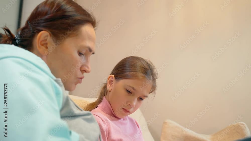 Mother with little daughter having fun and read the book together on the sofa at home. 10 year old girl with her mother reading a book. Love of family and concept Mother with little daughter having fun and read the book together on the sofa at home. 10 year old girl with her mother reading a book. Love of family and concept
