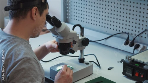 Radio electronic specialist examines the microchip using a digital microscope, adjusts the magnification. Worker uses an antistatic bracelet to avoid damage to high-precision equipment