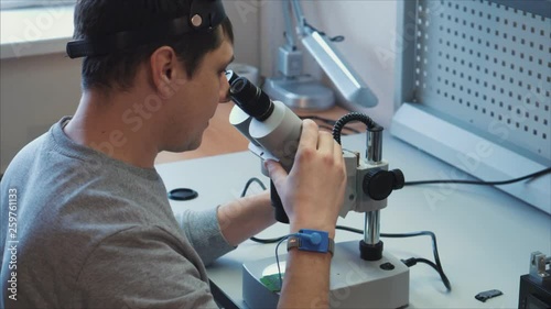 The inventor is testing a prototype that has just been manufactured, he uses a microscope to reveal flaws in the microchip. The concept of designing parts for robots