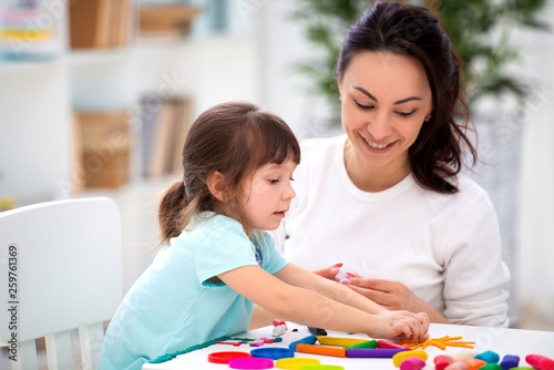Smiling mother helps a little daughter to sculpt figurines from plasticine. Children's creativity. Happy family