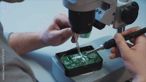 Closeup. A tech wunderkind repairing charger microcircuit from a professional camera using a soldering iron and tweezers.