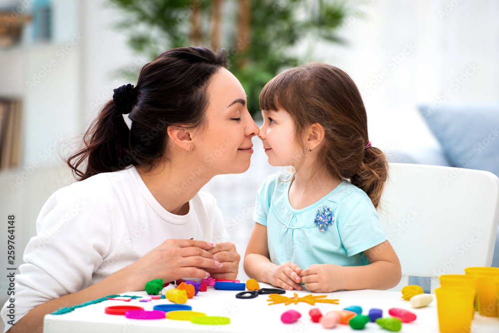 Mother's tenderness and love. Mom gently kisses her daughter in the nose. Woman and little girl mold from plasticine Mother's tenderness and love. Mom gently kisses her daughter in the nose. Woman and little girl mold from plasticine