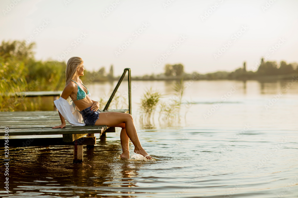 Young woman sitting on the pier on the lake