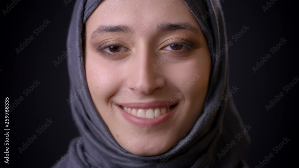 Closeup shoot of young attractive muslim female face in hijab looking at camera with smiling facial expression with background isolated on black Closeup shoot of young attractive muslim female face in hijab looking at camera with smiling facial expression with background isolated on black