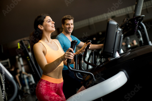 Young woman and man on elliptical stepper trainer exercising in gym