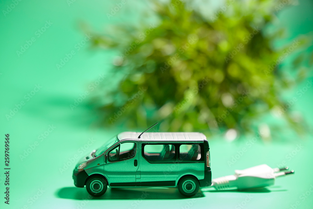 miniature of a vehicle with electric plug next to a plant on a green background miniature of a vehicle with electric plug next to a plant on a green background