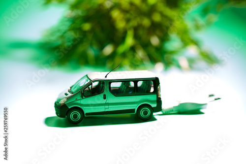 Fototapeta Naklejka Na Ścianę i Meble -  miniature of a vehicle with electric plug next to a plant on a green background