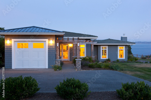 Contemporary house and garage at dusk with exterior lighting and lights on inside. Home energy use, water view real estate.