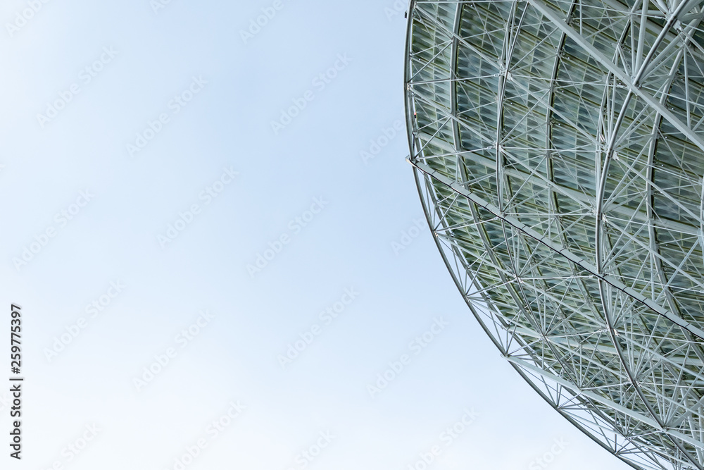 Huge white radio satellite dish isolated against a bright blue sky