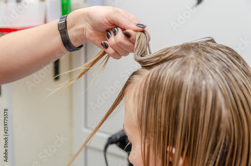 Hairdresser is cutting blond hair in hair salon. Trimming processes at the hair salon