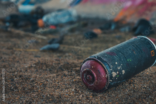 A discarded spray paint can among other littered objects around a graffiti wall.