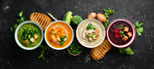 Assortment of colored vegetable cream soups. Dietary food. On a black stone background. Top view. Free copy space.