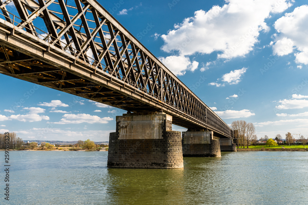 Steel, lattice structure of a railway bridge over a river with a background of blue sky with white clouds in western Germany.
