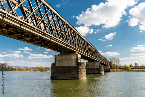 Steel, lattice structure of a railway bridge over a river with a background of blue sky with white clouds in western Germany.