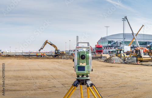 Surveyor engineer with equipment (theodolite or total positioning station) on the construction site of the road or building with construction machinery background