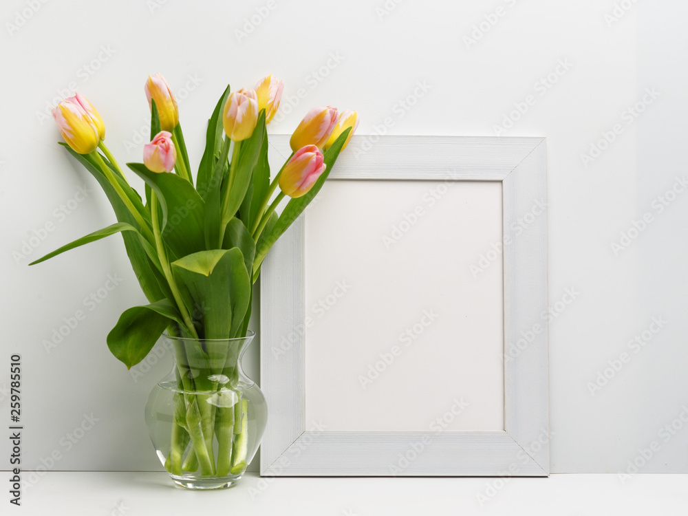Wooden frame on the table with a bouquet of delicate pink tulips in a glass vase. Copy space.