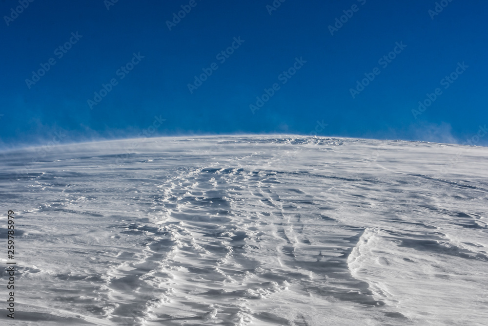 Wind storming and moving snow with a blue sky background, Passo Giau, Cortina d'Ampezzo, Dolomites, Italy